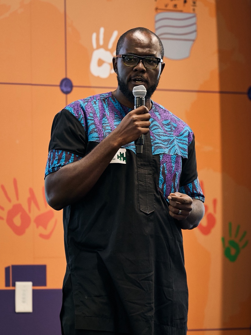 Bryan on stage with a microphone, pitching OwlReader in a black tunic with a blue and purple patterned yoke